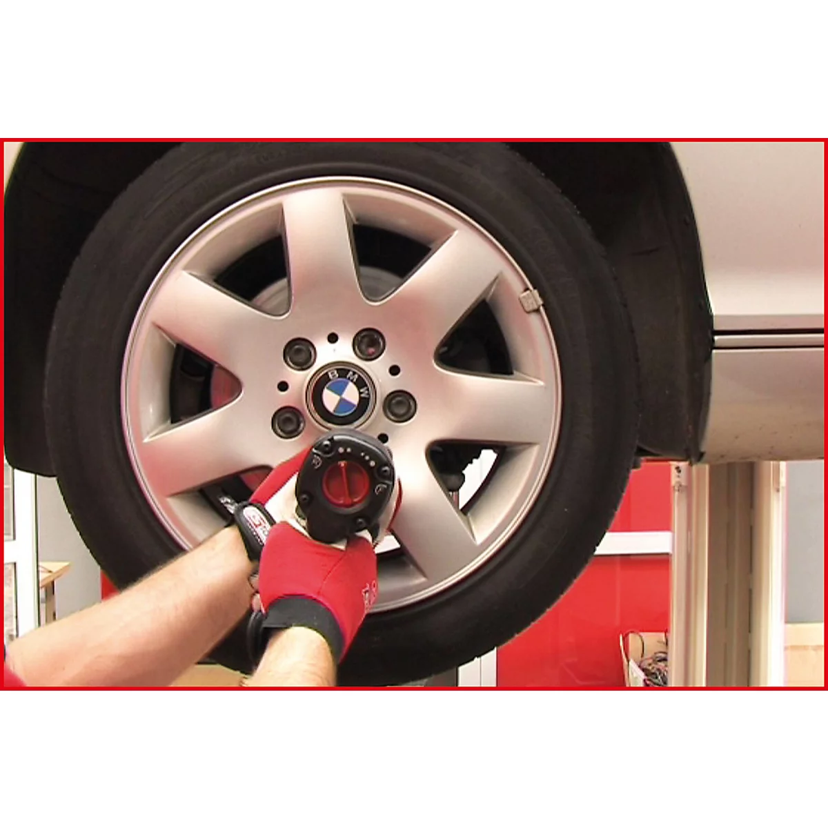 Ein Mann verschraubt mit einem Schlagschrauber ein Rad an einem BMW. Der Reifen und die Felge sind silberfarben. Der Mann trägt rote Handschuhe.